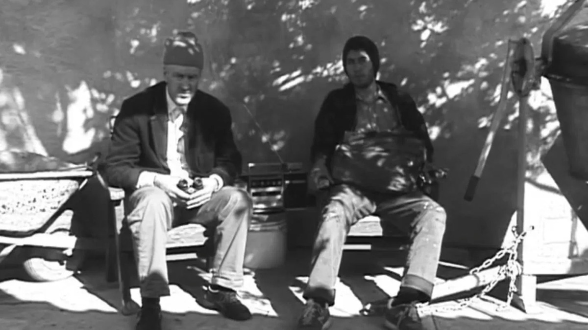 Prizor iz filma. Dva moška sedita zunaj.