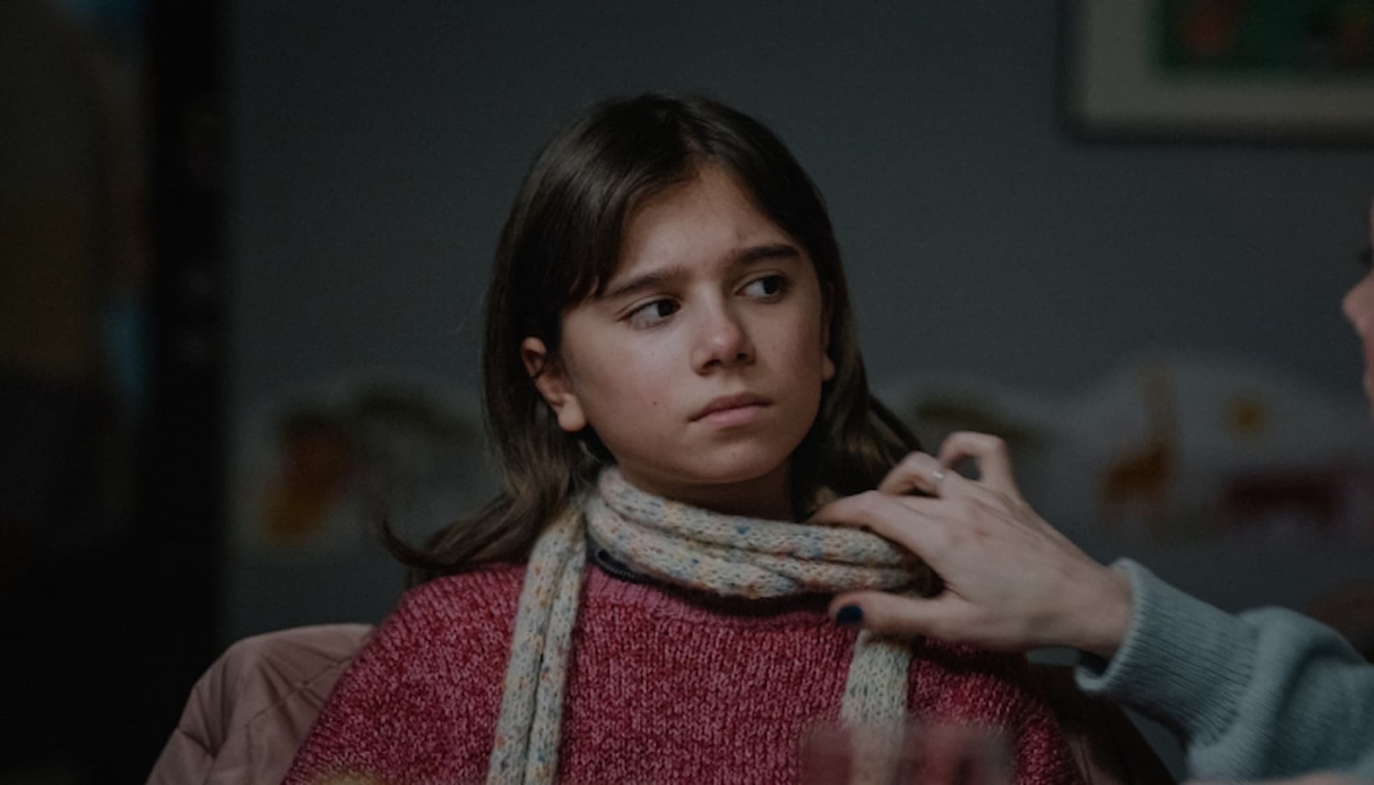Prizor iz filma. Deklici nekdo z roko odmika njen šal.